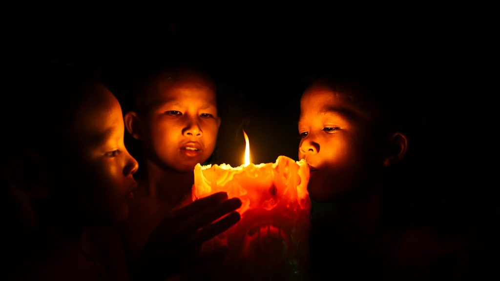 Young monks gather around a candle at Angkor Wat, Cambodia